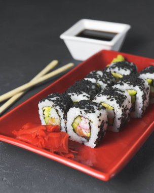 Lezzetli ve taze suşi seti ahşap çubuklarla kırmızı bir tabakta servis ediliyor. Yakın plan, suşi üzerine seçici odaklanma. Kaliforniya ya da Philadelphia suşi seti. Japon mutfağı kavramı.