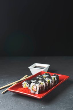 Lezzetli ve taze suşi seti ahşap çubuklarla kırmızı bir tabakta servis ediliyor. Yakın plan, suşi üzerine seçici odaklanma. Kaliforniya ya da Philadelphia suşi seti. Japon mutfağı konsepti. Boşluk afişini kopyala.
