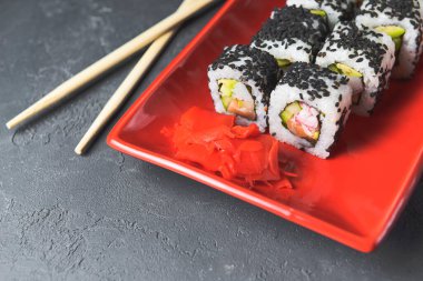 Lezzetli ve taze suşi seti ahşap çubuklarla kırmızı bir tabakta servis ediliyor. Yakın plan, suşi üzerine seçici odaklanma. Kaliforniya ya da Philadelphia suşi seti. Japon mutfağı konsepti. Boşluk afişini kopyala.