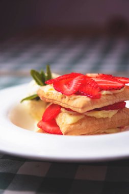 Pudra şekerli lezzetli çilekli börek ve bir kepçe vanilyalı dondurma. Yeşil ekose masa örtüsünün üzerinde beyaz bir tabakta servis ediliyor..