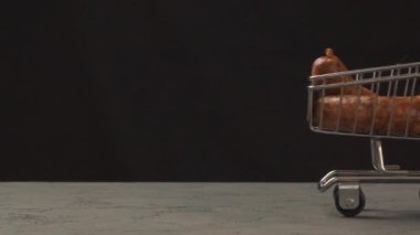 Küçük bir alışveriş arabası ve sosisler. Teslimat konsepti, siyah arkaplan üzerinde. Barbekü ızgara sosis. Dünya çapında Covid-19 salgınında yaratıcı reklam kavramı