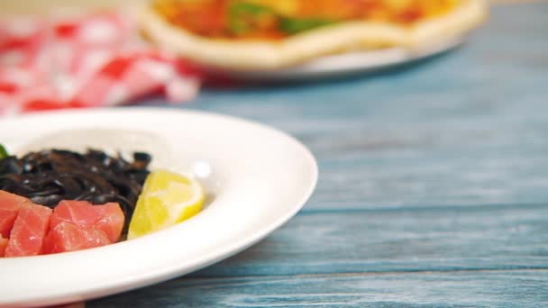 鮭の魚と黒イカインクパスタ レモン 木製のテーブルの上に白いプレートにバジル 白ワインのグラスで提供します カメラはゆっくりと皿の上を動く クローズアップ 高品質 — ストック動画
