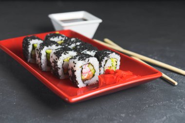 Lezzetli ve taze suşi seti ahşap çubuklarla kırmızı bir tabakta servis ediliyor. Yakın plan, suşi üzerine seçici odaklanma. Kaliforniya ya da Philadelphia suşi seti. Japon mutfağı kavramı.