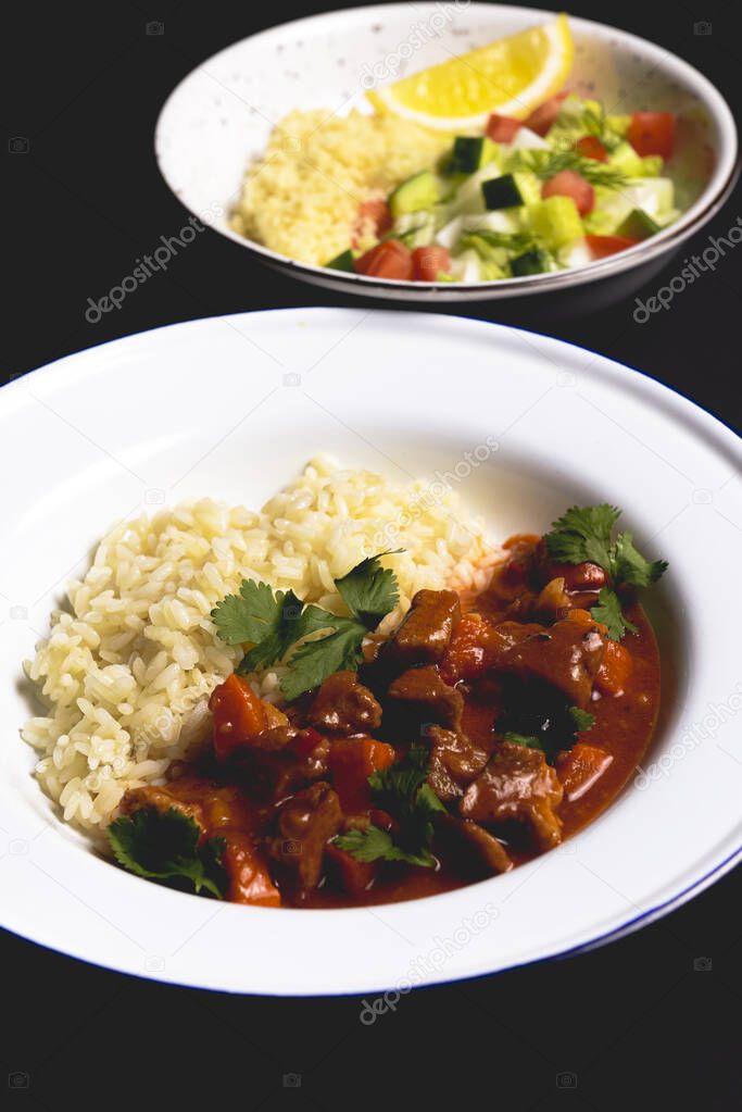 Chicken gravy with rice served in a white plate over black background. Tasty dinner idea, healthy eating.