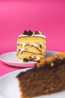 Fıstıklı kek, fındıklı pandispanya keki ve beyaz tabakta bir parça çikolatalı pasta. Pembe arka planda iki parça taze pişmiş kek. Tatlı zamanı..