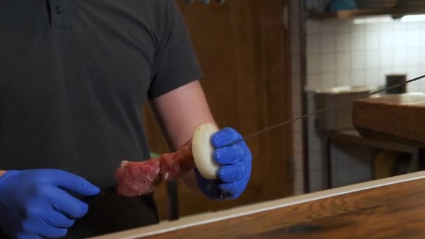 Chef faire un kebab sur la brochette, mettre de la viande crue sur la brochette. À l'intérieur, chef travaillant dans la cuisine, processus de travail. — Video