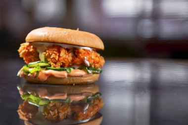 Yansıyan yüzeyde bir masada tavuk burger. Sebzeli tavuk burger ve bulanık arka plan. Fast food, abur cubur konsepti. Alan afişini ve web tasarımını kopyala.