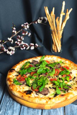 Etli, mantarlı, domatesli ve fesleğenli Rustik pizza. Ahşap masanın üzerinde, koyu renkli bir fotoğraf. İtalyan mutfağı, fast food, abur cubur.