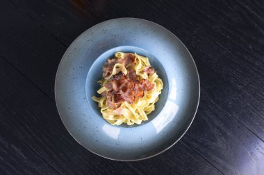 Carbonara spagettisi, koyu ahşap bir masada servis edilir. Geleneksel İtalyan Carbonara makarnası tarifi.