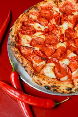 Sıcak Chilli Pepperoni Pizza, yemek için hazır. Kırmızı masa arkasındaki restoranda servis edilen kırmızı biberli, dilimlenmiş salamlı pizza..
