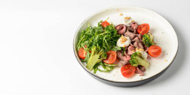 Beyaz arka planda servis edilen et, kiraz domatesleri, brokoli, keçi peyniri ve taze roka salatasından yapılmış sağlıklı bir salata. Lezzetli öğle yemeği ya da akşam yemeği fikri.