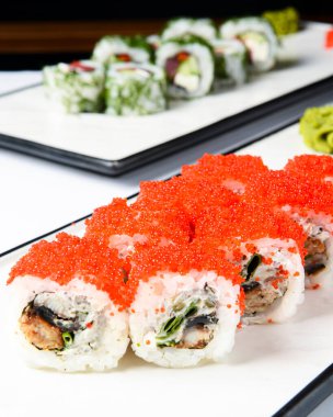 Kırmızı havyar ve krem peynirli suşi ruloları beyaz bir tabakta servis edilir. Geleneksel Japon mutfağı konsepti, suşi tarifi. Arka planda ton balıklı suşi ruloları..