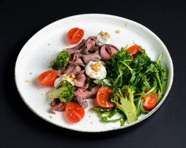 Etten, kiraz domatesinden, brokoliden, keçi peynirinden ve beyaz tabakta servis edilen taze roka suyundan yapılmış sağlıklı bir salata..