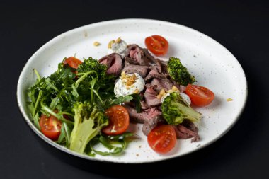 Etten, kiraz domatesinden, brokoliden, keçi peynirinden ve beyaz tabakta servis edilen taze roka suyundan yapılmış sağlıklı bir salata..