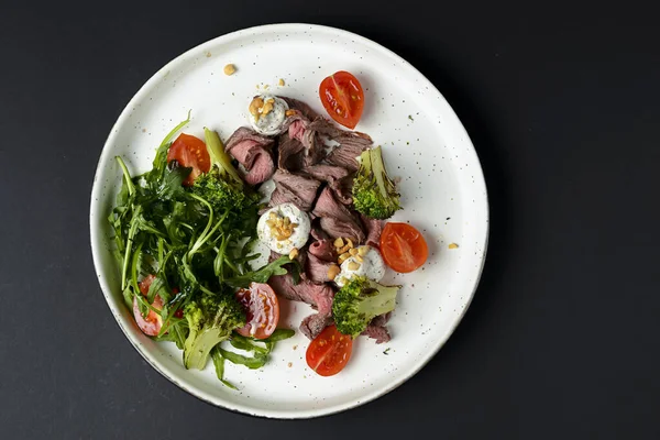 Etten, kiraz domatesinden, brokoliden, keçi peynirinden ve beyaz tabakta servis edilen taze roka suyundan yapılmış sağlıklı bir salata..