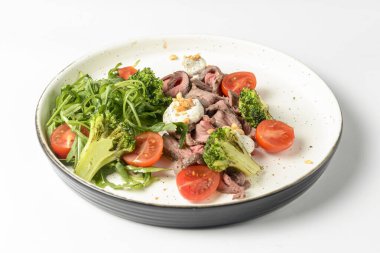 Beyaz arka planda servis edilen et, kiraz domatesleri, brokoli, keçi peyniri ve taze roka salatasından yapılmış sağlıklı bir salata. Lezzetli öğle yemeği ya da akşam yemeği fikri.