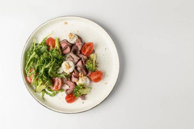 Beyaz arka planda servis edilen et, kiraz domatesleri, brokoli, keçi peyniri ve taze roka salatasından yapılmış sağlıklı bir salata. Lezzetli öğle yemeği ya da akşam yemeği fikri.