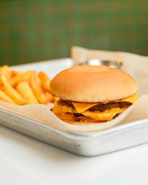 Restoranda metal tepside patates kızartması ve soslu hamburger, bulanık arka plan. Fast food, abur cubur konsepti. Dışarıda ye..