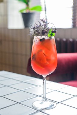 Lavanta ve böğürtlen kokteyli, restoranda veya barda beyaz bir masada uzun bir bardakta servis edilir. Dışarıda yemek konsepti. Parti için alkollü meyve sebzesi. Çiçeklerle süslenmiş. Kapat..