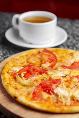 Tavuklu, domatesli ve mantarlı pizza yakın mesafede, bir pizzacıda ya da restoranda bir fincan çayla servis ediliyor. İtalyan mutfağı kavramı.
