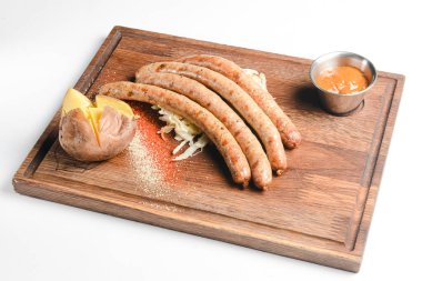 Sosisli ve fırında patatesli ahşap bir tahtanın üzerinde servis edilen bir yığın pişmiş sosis. Beyaz arka planda izole edilmiş. Ukrayna mutfağı kavramı.