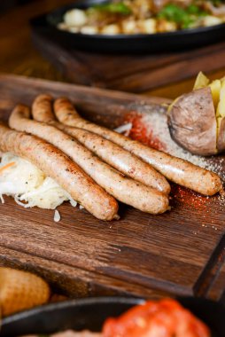 Ahşap bir tahtanın üzerinde sosis ve fırında patates ile servis edilen bir yığın pişmiş sosis. Ahşap bir masada servis ediliyor. Ukrayna mutfağı kavramı.