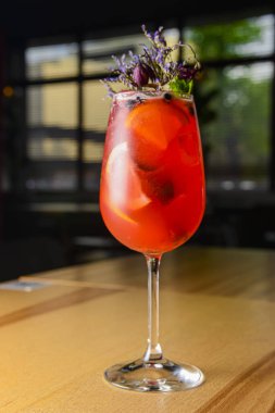 Lavanta ve dut kokteyli ahşap bir masada uzun bir bardakta servis edilir. Dışarıda yemek konsepti. Parti için alkollü meyve sebzesi. Çiçeklerle süslenmiş. Kapat..