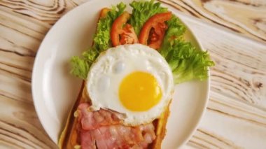Sabah kahvaltısı Belçika waffle 'ı yumurta, pastırma, domates ve marul salatası. Sabahları sağlıklı kahvaltı, yavaş çekim manzarası, yakın çekim. Tahta masanın üzerinde beyaz bir tabakta..