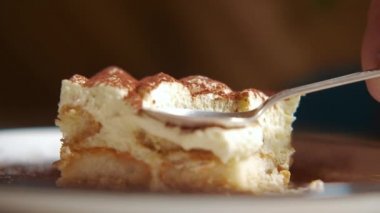 Kamera tiramisu kekinin üzerinde yavaşça hareket ediyor, tiramisu kekine odaklanıyor. Ağır çekim. Beyaz bir tabakta, ahşap bir masada tatlı geleneksel İtalyan tatlısı..