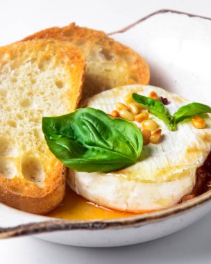 Beyaz arka planda beyaz bir kasede servis edilen soslu ve tostlu fırında camembert peyniri. Lezzetli yemek fikri, Fransız mutfağı konsepti, geleneksel tarif. Fırında peynirli camembert..
