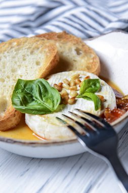 Beyaz ahşap zemin üzerinde beyaz bir kasede servis edilen soslu ve tostlu fırında camembert peyniri. Lezzetli yemek fikri, Fransız mutfağı konsepti, geleneksel tarif. Fırında peynirli camembert..