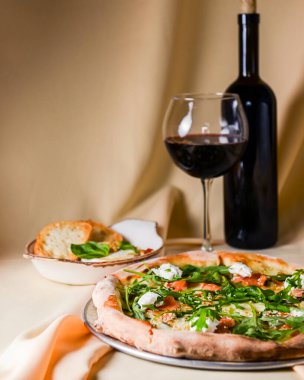 Mozarellalı pizza, somon dilimleri, taze roka. Fırında peynirli camembert ve kırmızı şarapla servis edilir. İtalyan mutfağı, geleneksel pizza tarifi..