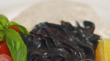 Somon balıklı siyah mürekkep balığı makarna, limon, ahşap masadaki beyaz tabakta fesleğen. Bir bardak beyaz şarapla servis edilir. Kamera çanağın üzerinde yavaşça hareket ediyor. Yakın çekim, yüksek kalite..