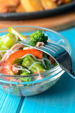 Brokolili sotelenmiş sebze salatası, kuşkonmaz, tatlı biber ve selofan erişte veya mavi arka planda cam bir kasede fensi eriştesi. Akşam yemeği fikri, kızarmış tavuklu biftek ve kızarmış patates..