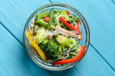 Brokolili sotelenmiş sebze salatası, kuşkonmaz, tatlı biber ve selofan erişte veya mavi arka planda cam bir kasede fensi eriştesi. Akşam yemeği fikri.