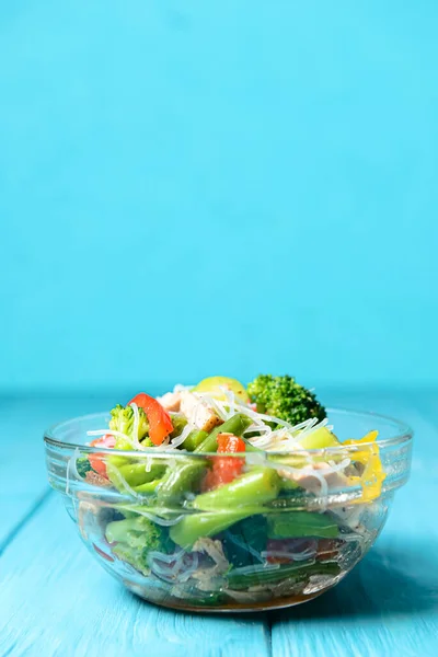 Brokolili sotelenmiş sebze salatası, kuşkonmaz, tatlı biber ve selofan erişte veya mavi arka planda cam bir kasede fensi eriştesi. Akşam yemeği fikri, uzay afişini kopyala.