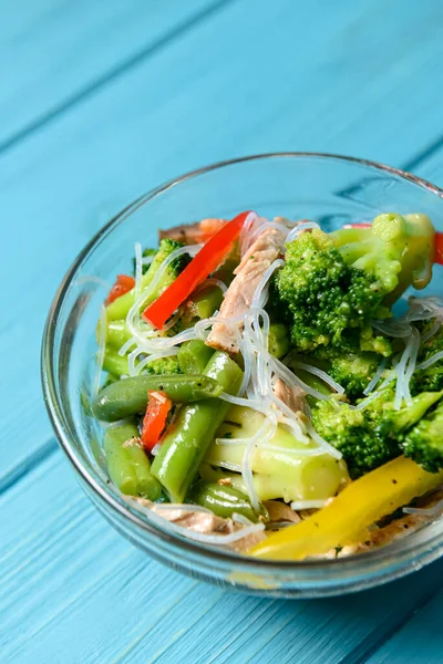 Brokolili sotelenmiş sebze salatası, kuşkonmaz, tatlı biber ve selofan erişte veya mavi arka planda cam bir kasede fensi eriştesi. Akşam yemeği fikri.
