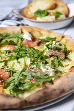 Mozarellalı pizza, somon dilimleri, taze roka. Fırında peynirli camembert ve kırmızı şarapla servis edilir. İtalyan mutfağı, geleneksel pizza tarifi..