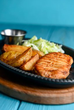 Kırsal tarzda kızarmış patatesli ızgara tavuk bifteği ve mavi arka planda servis edilen lahana salatası salatası. Akşam yemeği fikri.