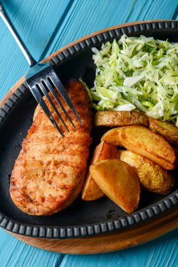 Kırsal tarzda kızarmış patatesli ızgara tavuk bifteği ve mavi arka planda servis edilen lahana salatası salatası. Akşam yemeği fikri.