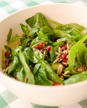 Domatesli ıspanak salatası, taze roka, kabak çekirdeği, yeşil ekoseli beyaz bir kasede servis edilen nar tohumları. İtalyan mutfağı kavramı.