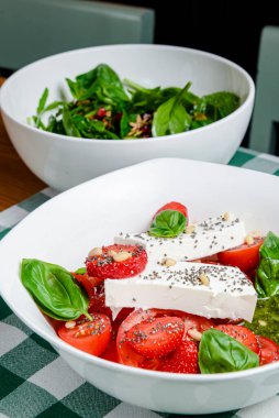 Çilekli Caprese salatası, mozzarelller, fesleğen ve balzamik sos yeşil ekose arka planda beyaz bir kasede servis edilir. İtalyan mutfağı konsepti, yaz menüsü, geleneksel çilekli tarifi..