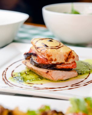 Fırında kavrulmuş ratatouille ile biberiye tavuğu yeşil ekose masa örtüsüyle beyaz kare bir tabakta servis edilir. İtalyan mutfağı, lezzetli yemek fikri..