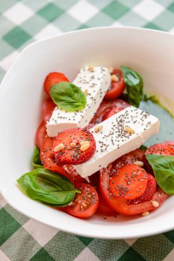 Çilekli Caprese salatası, mozzarelller, fesleğen ve balzamik sos yeşil ekose arka planda beyaz bir kasede servis edilir. İtalyan mutfağı konsepti, yaz menüsü, geleneksel çilekli tarifi..
