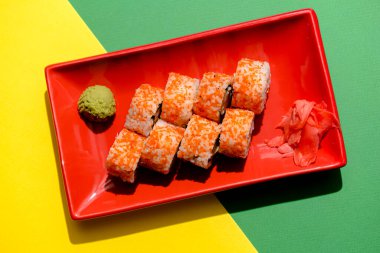 Kaliforniya suşi ruloları kırmızı bir tabakta servis ediliyor. Renkli yeşil ve sarı arka planda. Yakın çekim, suşi üzerine seçici odaklanma. Japon mutfağı konsepti. Geleneksel Kaliforniya suşi tarifi.