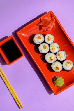 Japon suşi ruloları kırmızı bir tabakta turşulu zencefil ve wasabi sosuyla servis ediliyor. Japon mutfağı konsepti. Geleneksel suşi maki rulo tarifi.