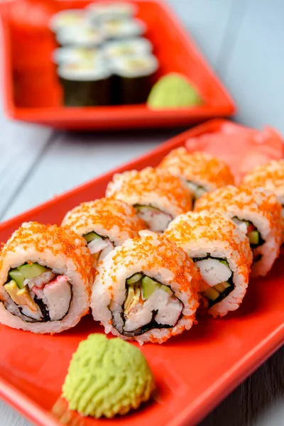 California sushi rolls served on a red plate over light wooden background. Close up, selective focus on sushi. Japanese cuisine concept. Traditional California sushi recipe.