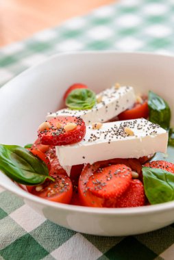 Çilekli Caprese salatası, mozzarelller, fesleğen ve balzamik sos yeşil ekose arka planda beyaz bir kasede servis edilir. İtalyan mutfağı konsepti, yaz menüsü, geleneksel çilekli tarifi..