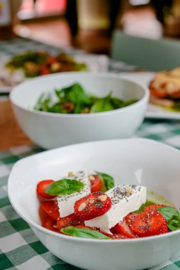 Çilekli Caprese salatası, mozzarelller, fesleğen ve balzamik sos yeşil ekose arka planda beyaz bir kasede servis edilir. İtalyan mutfağı konsepti, yaz menüsü, geleneksel çilekli tarifi..