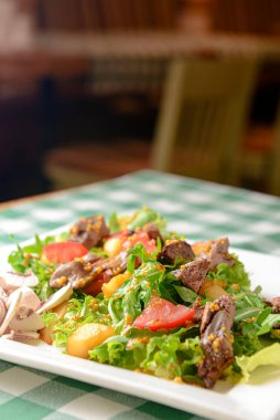 Sığır etli salata, domates, taze marul salatası ve roka, çiğ mantar ve dijon hardalından harika sos. Ekoseli masa örtüsü üzerine beyaz bir tabakta servis edilmiş. İtalyan mutfağı kavramı